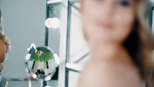 4K video Gordegous beautiful glamour woman looking at the mirror reflection  in beauty salon. Curly hairstyle and gala make up in white room.