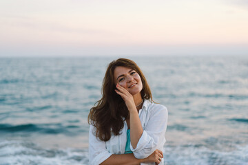 Fototapeta na wymiar Portrait of a happy young woman on a background of beautiful sea. The girl looks at the magical sea. Freedom and happiness