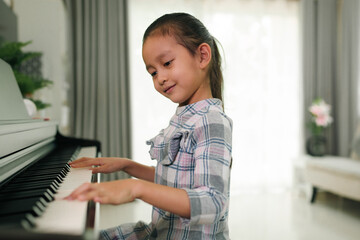 Cute asian 6 years old is practice playing piano at home and smiling with happiness moment, concept...