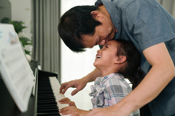 Asian father kissing daughter and smiling together with happy moment while playing piano at home,concept of love, bonding, relation, education, music, skill, mental health, parent and child in family  - Powered by Adobe