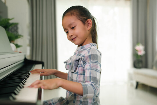 Cute asian 6 years old is practice playing piano at home and smiling with happiness moment, concept of learning, art, steam, musical, mental health, homeschool, skill, ability concept.