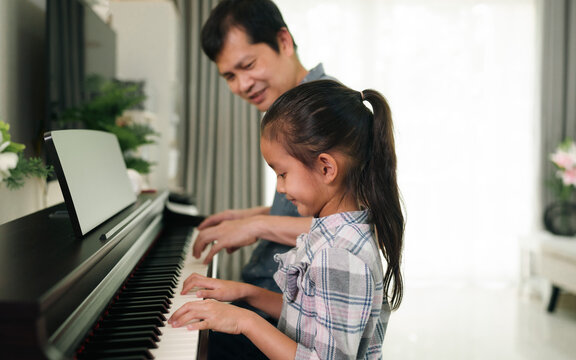 Asian daughter and father are playing electronic piano together with happy moment at home, concept of love, bonding, relation, education, music, skill, mental health, parent and child in family life.