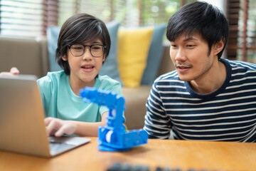 asian boy child with father successful control robot arm on Digital tablet and computer keyboard, happy family getting a lesson in coding control robotics at home.study at home concept.