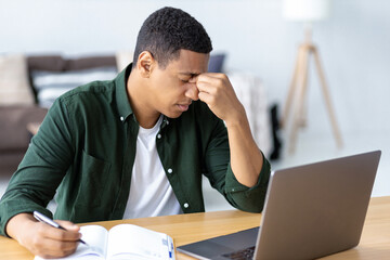 Close-up portrait of tired stressed African American man having headache feeling sick. sitting at the workplace in the office. Male suffering from migraine and overwork