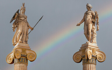 A rainbow over Athena and Apollo marble statues on Ionic style columns. Athens, Greece.