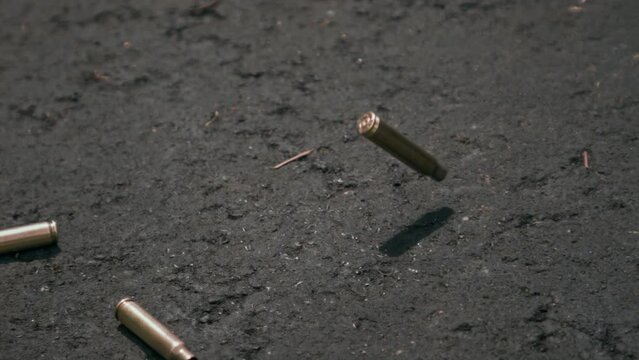 Empty bullet shell casings falling on asphalt ground in 1000fps slow motion