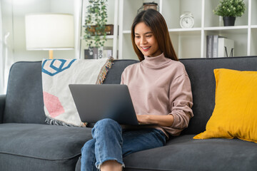 Cheerful young woman sitting on sofa and using laptop computer at home.