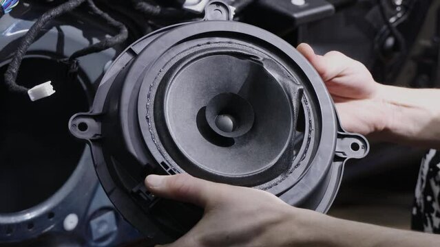 Man shows torn loud speaker taken out of car door. Specialist holds detail in hands removing diffuser. Process of stock speaker replacement closeup