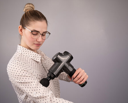 Caucasian business woman massaging her biceps with a percussion massager.