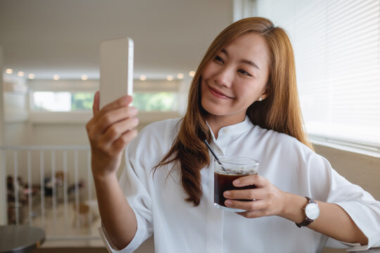 Portrait image of a beautiful young asian woman using mobile phone to take a selfie while drinking coffee in cafe