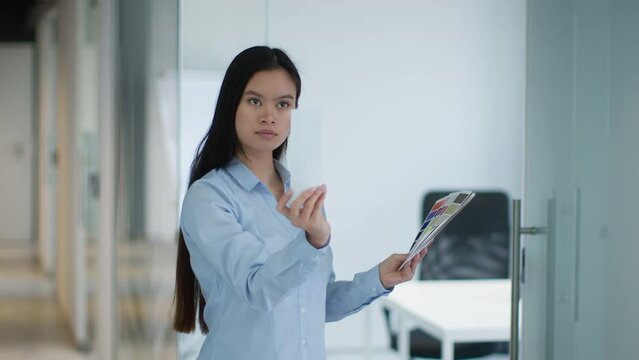 Young professional asian woman interior designer standing with color swatches, choosing style for office renovation