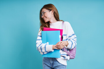 Naklejka premium Cheerful female student carrying workbooks while standing against blue background