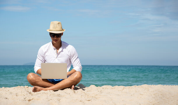 Handsome relaxed man using laptop, beach background, freelance working social on holiday summer. Summer and Vacation Concept