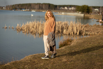 Happy beautiful blonde woman walking along river bank alone on cool sunny day, relaxing, meditating and enjoying peace and freedom. Outdoors weekend activity, rural landscape, nature background