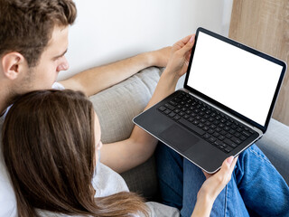 Home rest. Happy couple. Computer mockup. Relaxed beloved man and woman watching laptop with blank screen in light room interior.