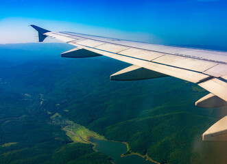 View of airplane wing, blue skies and green land during landing. Airplane window view.