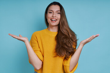Beautiful young woman gesturing and looking at camera while standing against blue background