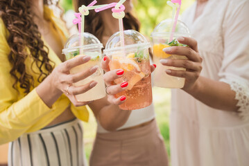 Fototapeta premium Plastic disposable cups with refreshing drinks close-up. Girls toast glasses with cocktails. Unrecognizable group of people
