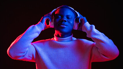 Music banner. Playlist joy. Millennial lifestyle. Satisfied delighted chill man in headphones enjoying song in bright red blue neon light dark background.