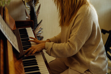 Beautiful blonde woman in home clothes sitting at piano, pressing chord and playing melody top...
