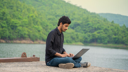 Young man working on a laptop and sitting in the nature, Workation and Digital Nomad concept.