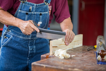 A carpenter works with equipment on a wooden table in a carpentry shop.