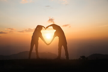 A woman and a man make a heart at sunrise on the mountain. god is love concept heart shape mountain...
