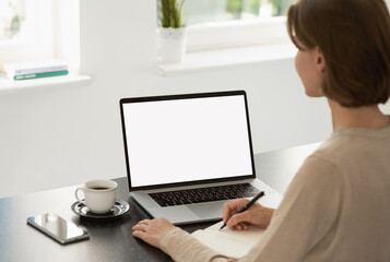 Fototapeta premium Young woman using laptop computer at home. Blank empty white mockup screen. Freelance, student lifestyle, online learning, meeting, web conference, video call, technology concept