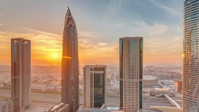 Sky view to skyscrapers during sunset in Dubai downtown aerial timelapse. Modern architecture with orange clouds and traffic on a highway. City walk district on a background