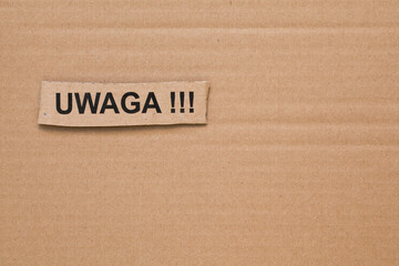 Cut out piece of cardboard with the words "UWAGA!!!" written on it. Brown cardboard in the background..