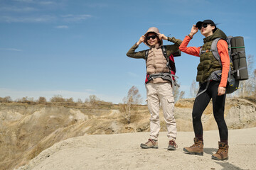 Horizontal long shot of two young Asian women wearing backpacks hiking in quarry on sunny spring day