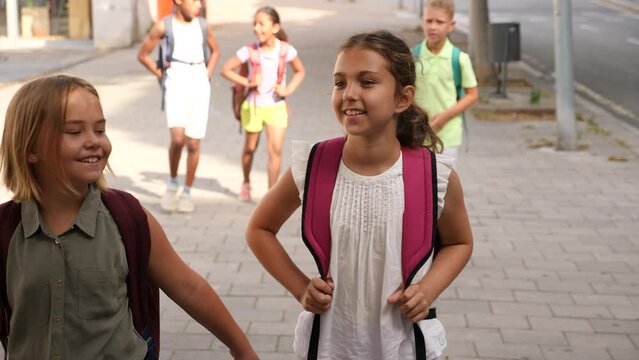 Schooldgirls walking together in schoolyard. They're classmates walking behind them.