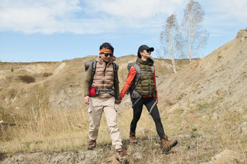 Horizontal long shot of two modern young Asian women spending weekend together hiking holding hands