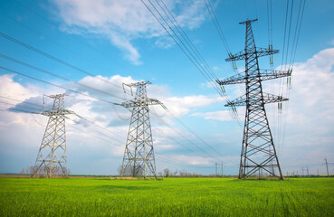 High voltage lines and power pylons in a flat and green agricultural landscape on a sunny day with...