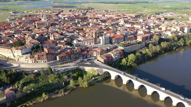 Picturesque aerial view of Tordesillas townscape on Duero river overlooking brownish tiled roofs of residential buildings and temples on spring day, Spain
