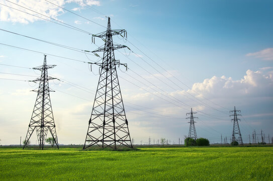 High voltage lines and power pylons in a flat and green agricultural landscape on a sunny day with clouds in the blue sky. Cloudy and rainy. Wheat is growing