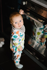 The baby learns to stand near the oven in the kitchen. Little nine months baby boy stands with support at home. Toddler just learnt how to stand on her feet. Baby taking first steps.