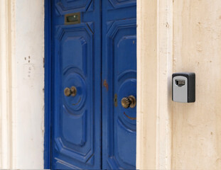 Smart key lock mounted on wall for renting apartment. Safe Key Box is used when the guest arrives at the touristic flat and the host can't open the door. Safe access to living space. Blue vintage door