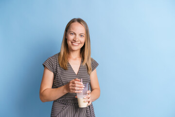 Happy woman in gray dress stands with milkshake in her hands and smiles with white teeth. Health...