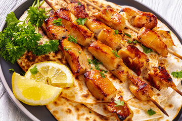 grilled chicken kebabs sprinkled with chopped fresh parsley over flatbreads on plate on white...