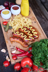 Tasty freshly grilled Sausages served with French fries and sauce on wooden board