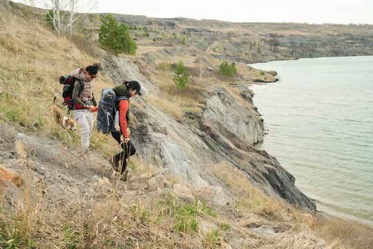 Horizontal long shot of two young Asian women hiking together with dog going down the quarry slope