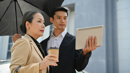 Asian aged businesswoman with male assistant, checking her building at the construction site.