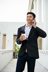 Smart Asian businessman in formal suit standing outside the building and talking on the phone.