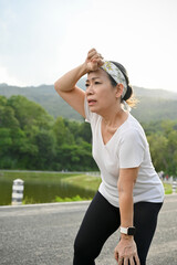 Exhausted asian aged woman taking a break after had a long jogging in the park.