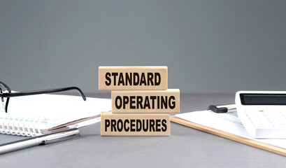 STANDARD OPERATING PROCEDURE text on wooden block with notebook,chart and calculator, grey...