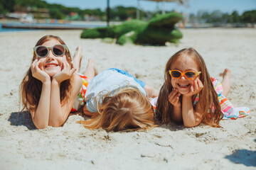 three happy children lie on the sand on the beach.a child with down syndrome with friends has fun...