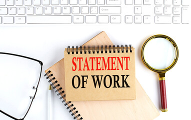 STATEMENT OF WORK text in the office notebook with keyboard, magnifier and glasses , business...