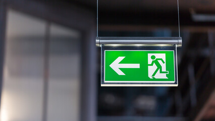 Illuminated emergency exit sign. Arrow pointing to the left. - obrazy, fototapety, plakaty