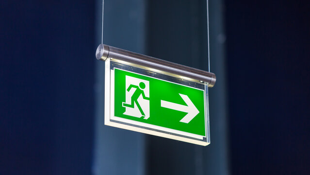 Essen, Germany - Mar 26, 2022: Emergency exit sign. With running figure, arrow pointing to the right. Blurry background.